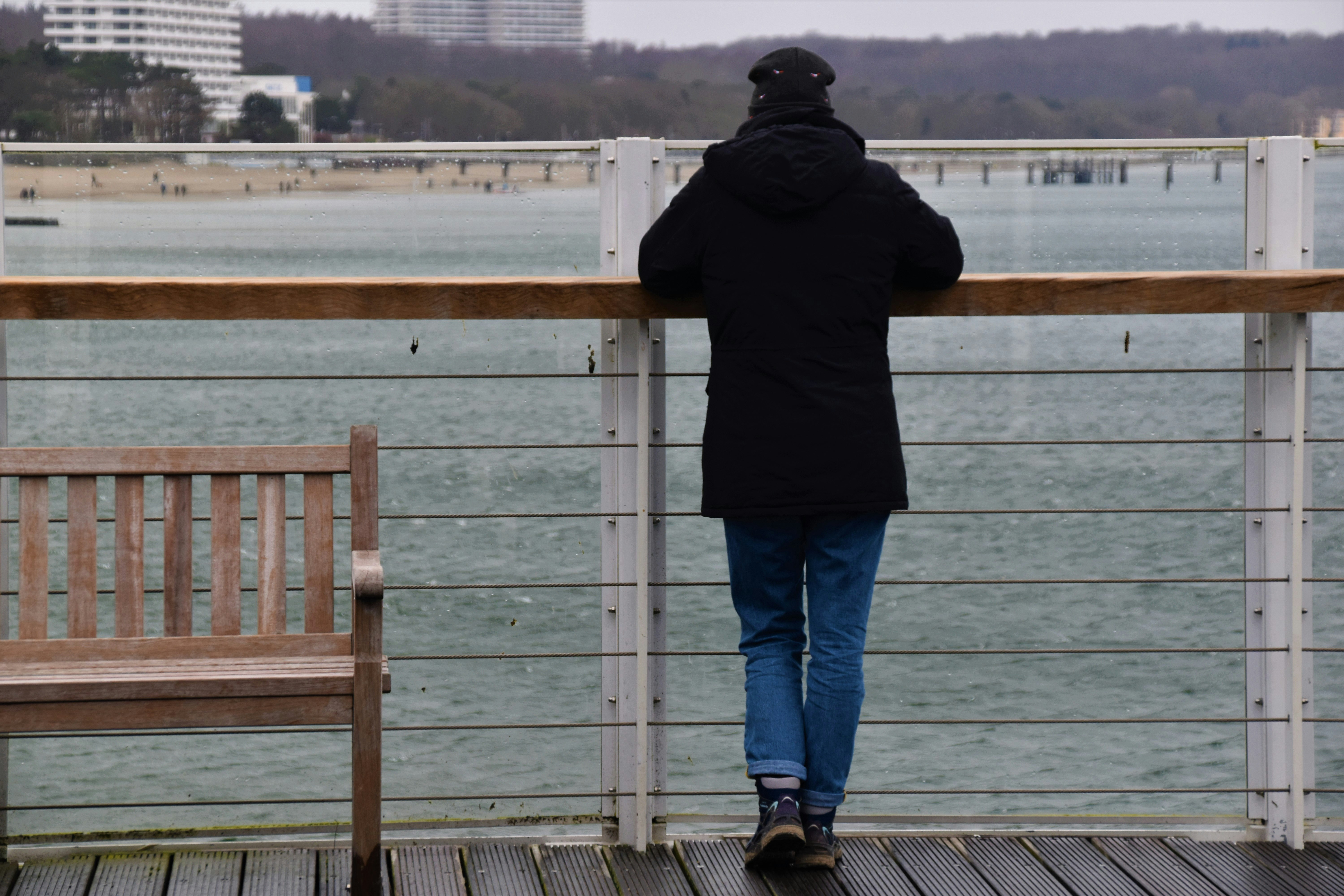 man in black hoodie and blue denim jeans standing on dock during daytime